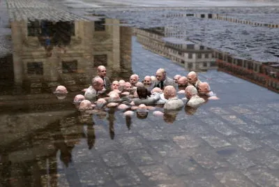 The image shows an art installation where politicians stand in a puddle, symbolising how the water level, or sea level, rises around them while they talk.